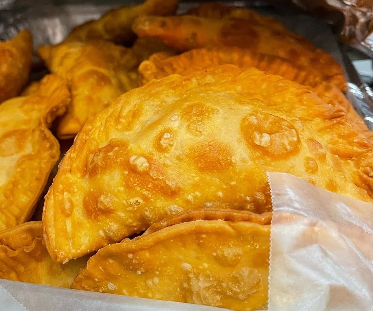 Close-up of golden, bubbly KDM empanadas in a foil-lined container